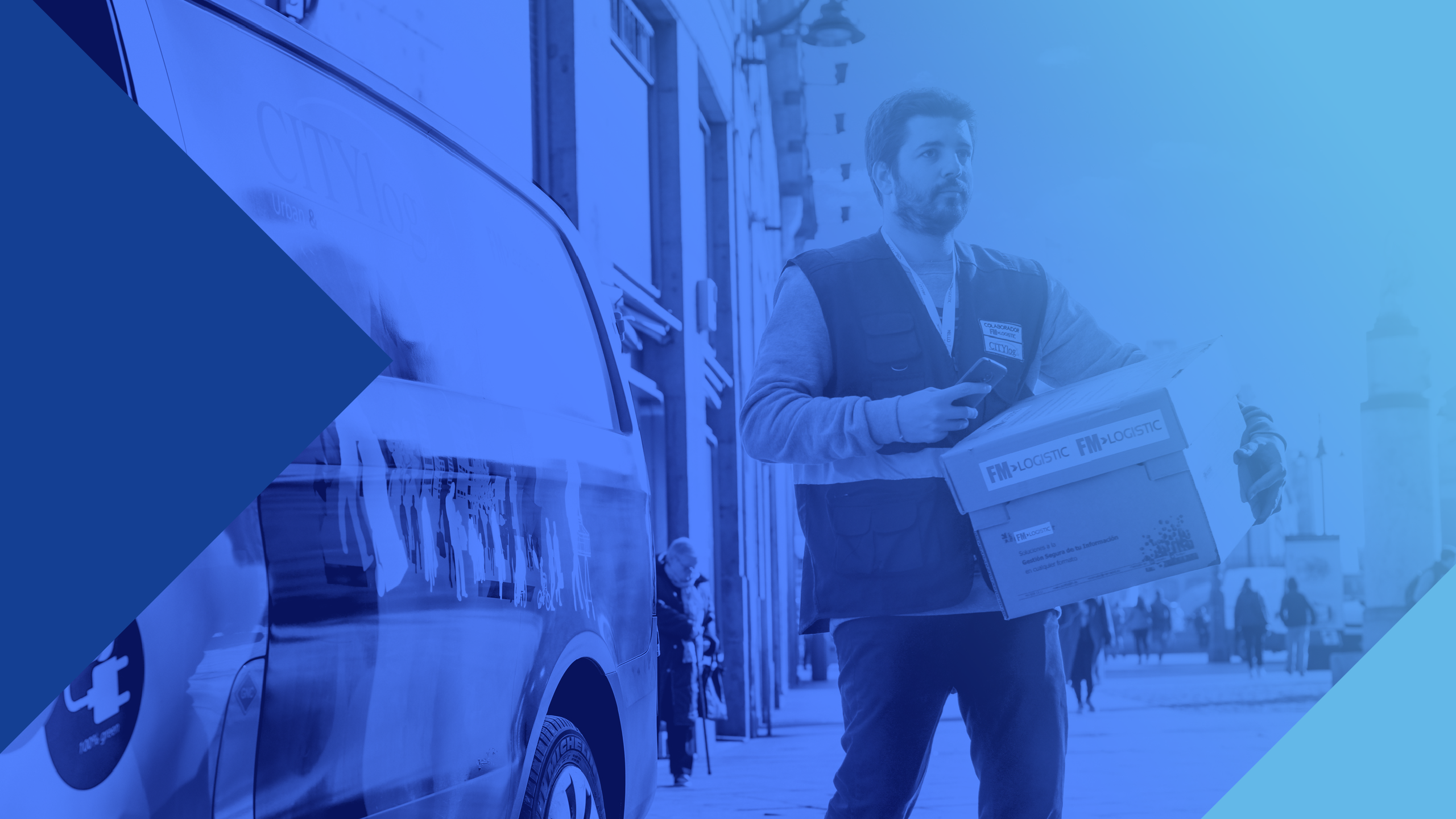 Man on a busy city street standing next to a delivery van, carrying a box that has an FM Logistics sticker on the side